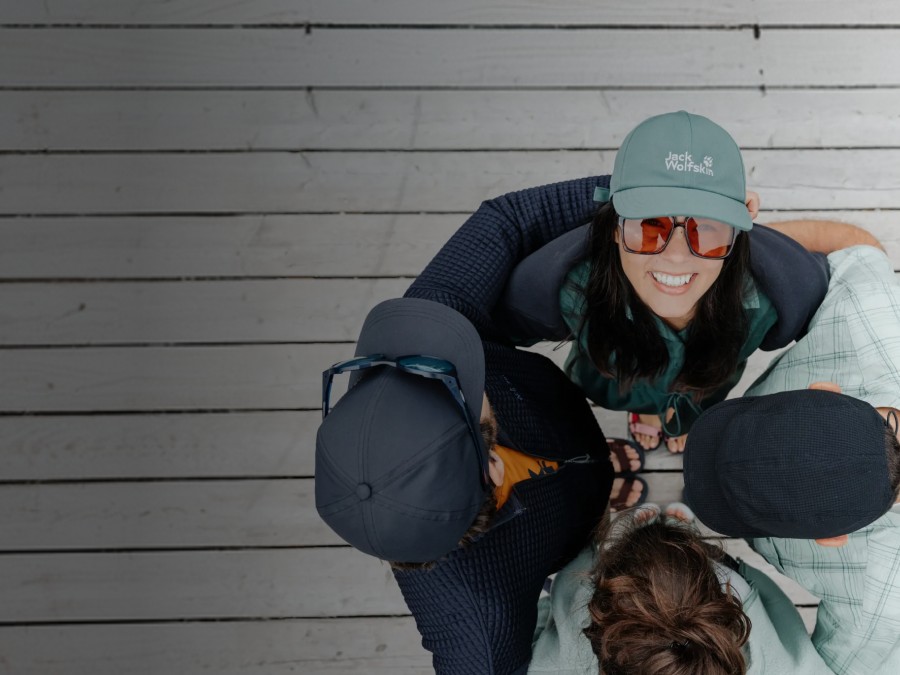 Two sleds with two people each are riding down a snowy slope. The people are laughing and wearing winter clothing, hats, and sunglasses; snow-covered mountains can be seen in the&nbsp;background.