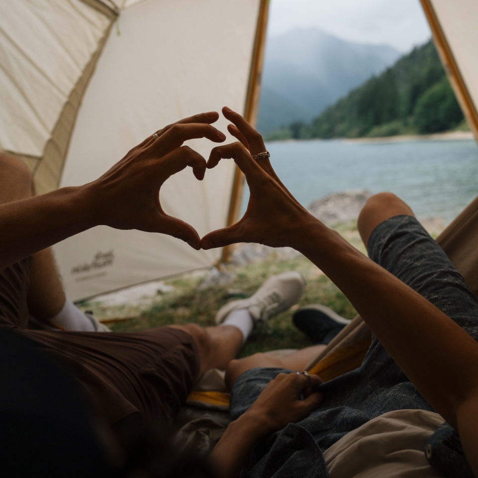 Two people in a tent and forming a heart with their hands